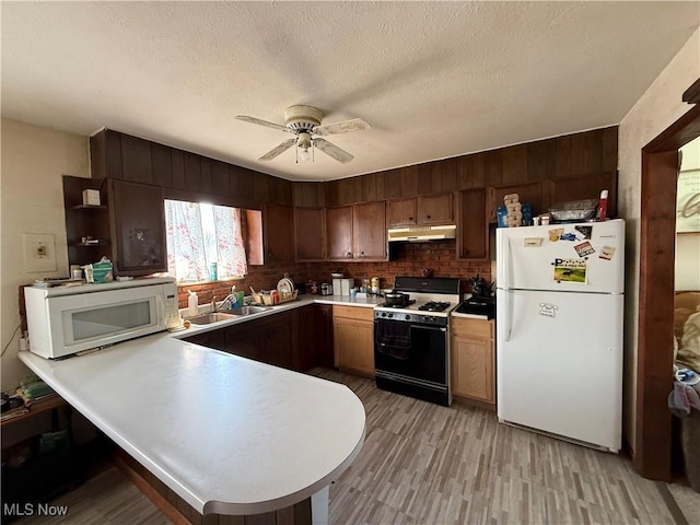 kitchen featuring under cabinet range hood, light countertops, a peninsula, white appliances, and a sink