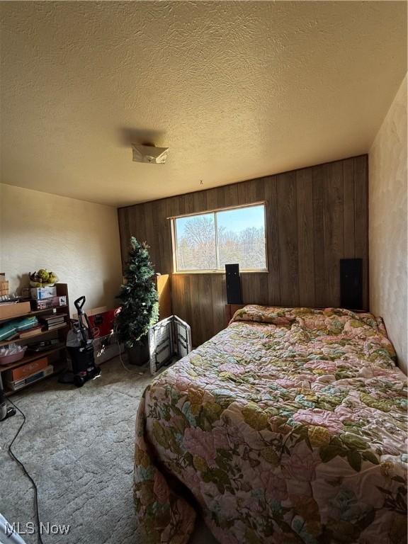 carpeted bedroom featuring wood walls and a textured ceiling