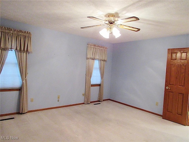 empty room featuring a ceiling fan, light colored carpet, baseboards, and a textured ceiling