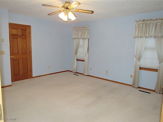 spare room featuring visible vents, light carpet, baseboards, and a ceiling fan