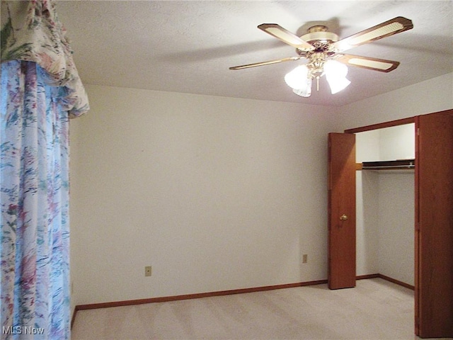 unfurnished bedroom featuring a closet, light colored carpet, a ceiling fan, and baseboards