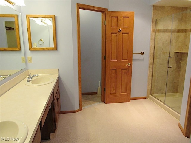 full bathroom with double vanity, a shower stall, baseboards, and a sink