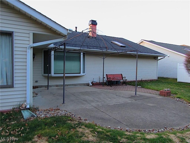 back of property featuring a lawn, a chimney, and a patio