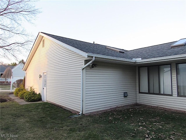 view of home's exterior with a lawn and a shingled roof