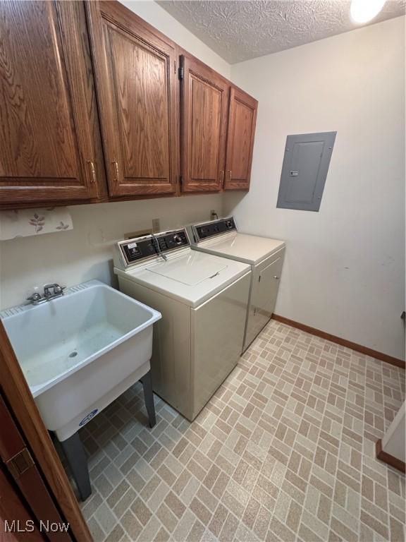 laundry room featuring washing machine and clothes dryer, baseboards, electric panel, cabinet space, and a sink