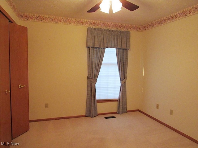 empty room featuring light carpet, visible vents, a ceiling fan, and baseboards