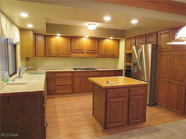 kitchen with light wood finished floors, a kitchen island, recessed lighting, brown cabinets, and appliances with stainless steel finishes