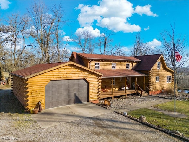 log home with log siding, covered porch, driveway, and an attached garage