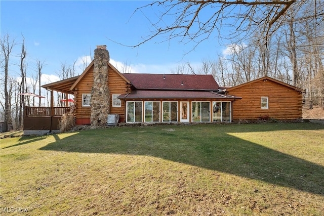 rear view of house with log siding, a chimney, a yard, and a sunroom