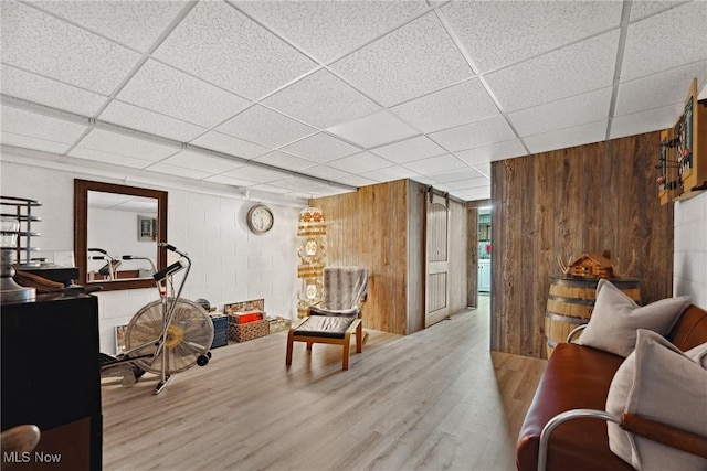 interior space featuring a drop ceiling, concrete block wall, wood finished floors, and wood walls