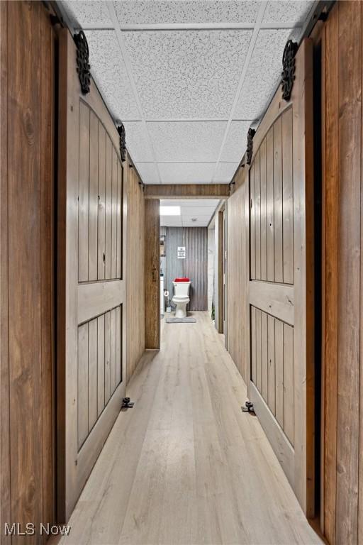 hall with a drop ceiling, wood finished floors, wood walls, and a barn door