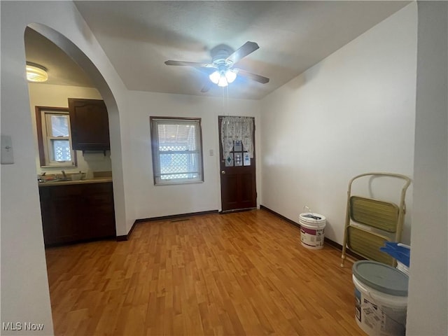 foyer entrance with arched walkways, light wood-style flooring, a healthy amount of sunlight, and ceiling fan