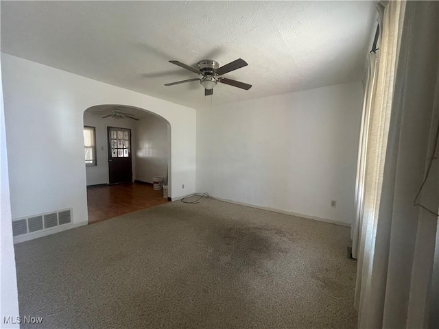 empty room with visible vents, a ceiling fan, a textured ceiling, arched walkways, and carpet floors