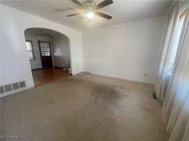 unfurnished room with visible vents, arched walkways, carpet floors, and a ceiling fan