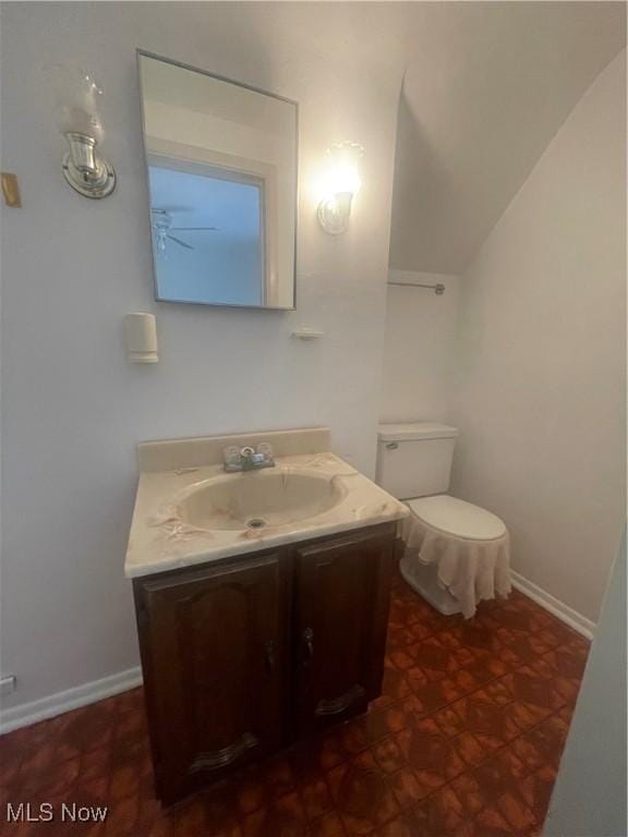 half bath featuring baseboards, toilet, vanity, and vaulted ceiling