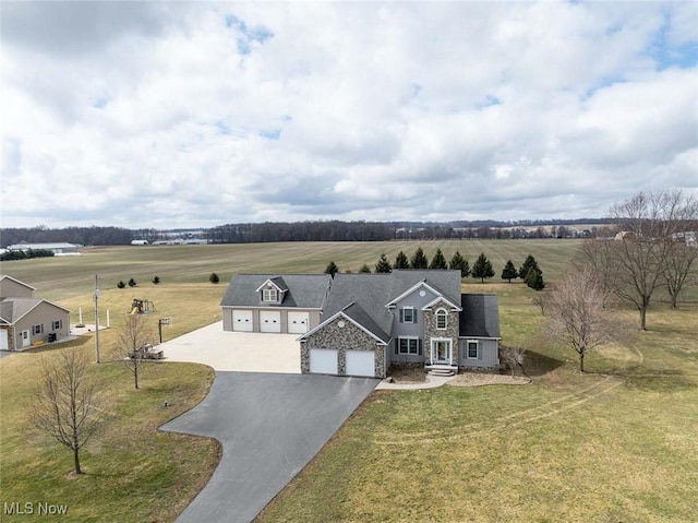 view of front of house featuring stone siding, a front yard, a rural view, and driveway