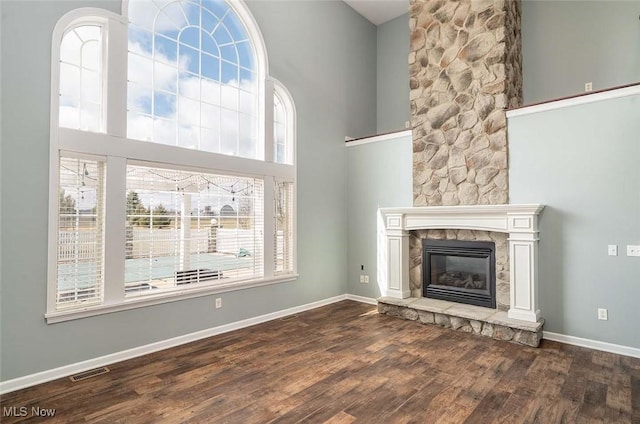 unfurnished living room featuring visible vents, wood finished floors, a towering ceiling, and a glass covered fireplace