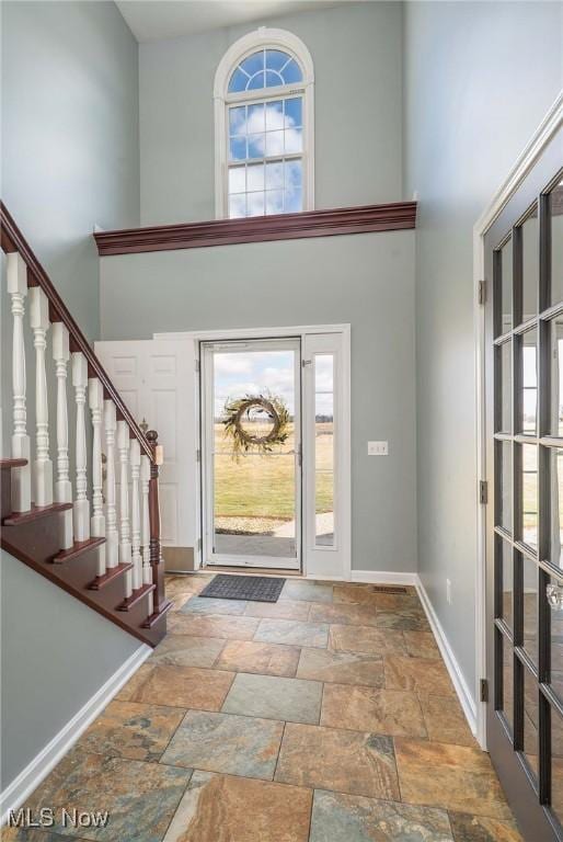 entrance foyer with stone finish floor, stairs, baseboards, and a towering ceiling