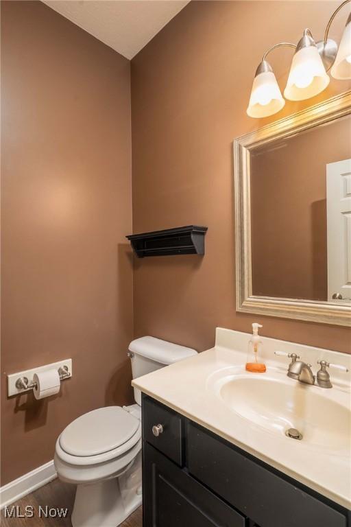 half bathroom with toilet, vanity, and baseboards