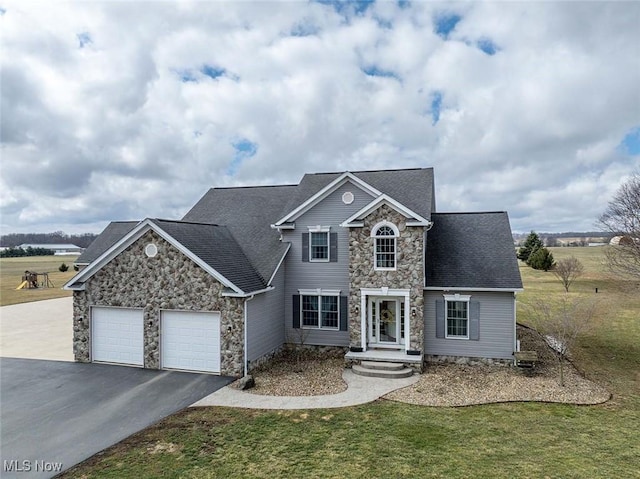 traditional home featuring a front yard, driveway, an attached garage, a shingled roof, and stone siding