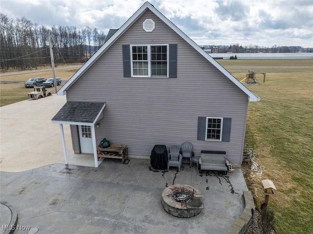 rear view of property with a yard, a patio, a shingled roof, and an outdoor fire pit