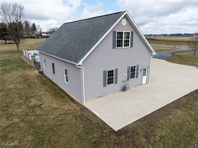 view of side of home with a yard, roof with shingles, concrete driveway, and a patio area