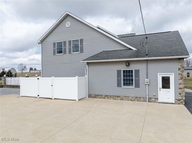 rear view of property with fence, a shingled roof, and a patio area