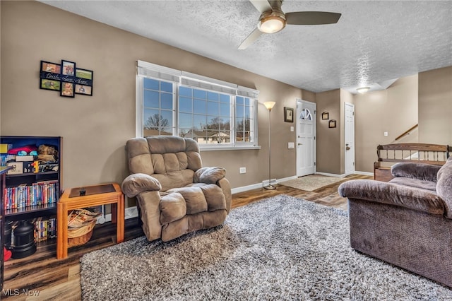 living room featuring ceiling fan, a textured ceiling, baseboards, and wood finished floors