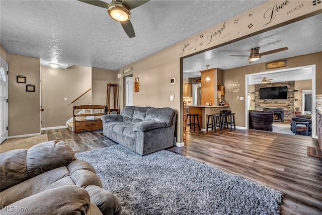 living area with ceiling fan, a textured ceiling, baseboards, and wood finished floors