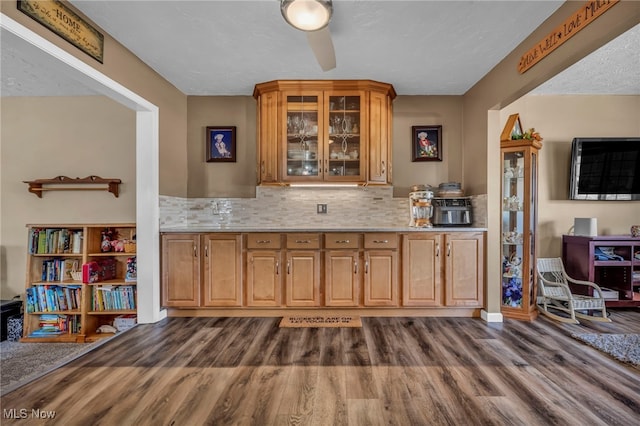 kitchen with glass insert cabinets, brown cabinets, tasteful backsplash, and dark wood-style flooring