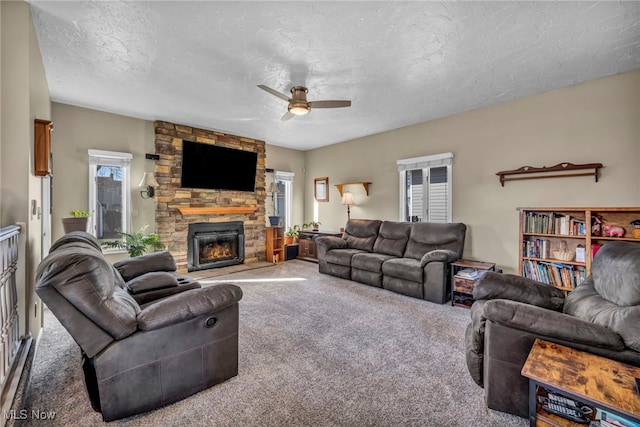 carpeted living room with a stone fireplace, plenty of natural light, a ceiling fan, and a textured ceiling