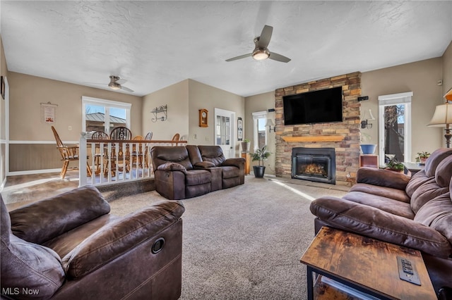 carpeted living area with a stone fireplace, ceiling fan, and a textured ceiling