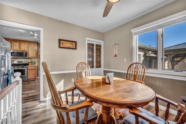 dining area with a ceiling fan, dark wood-style floors, wood walls, and wainscoting