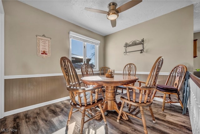 dining space featuring a textured ceiling, ceiling fan, wood finished floors, and wainscoting