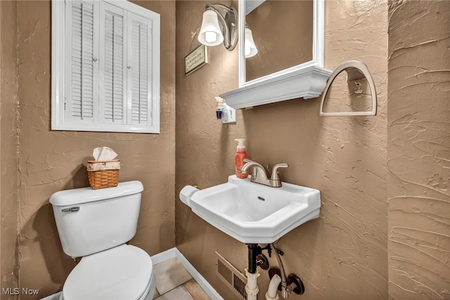 bathroom featuring a sink, toilet, and a textured wall