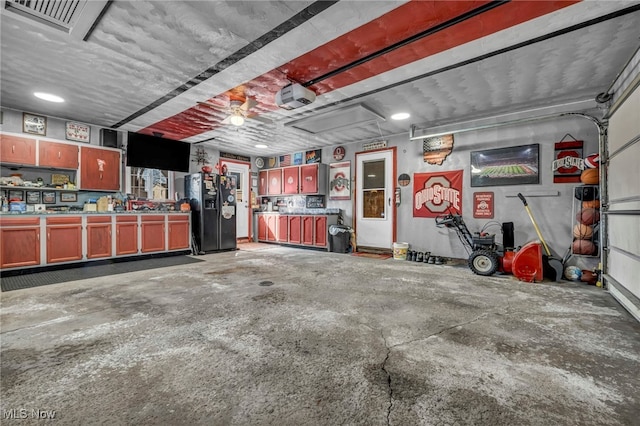 garage featuring black fridge with ice dispenser, a garage door opener, and visible vents