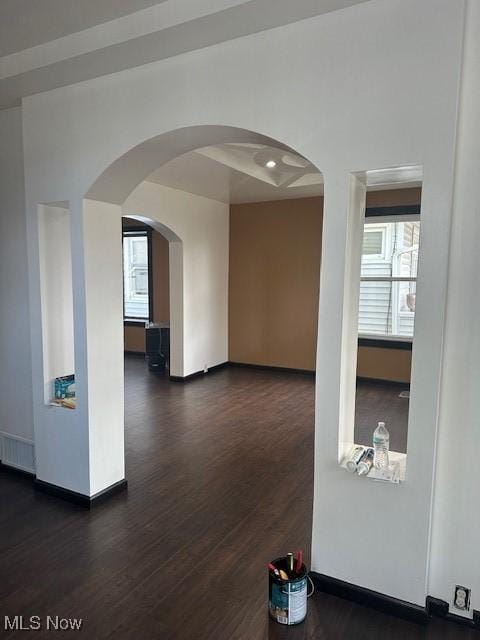 unfurnished room featuring baseboards, arched walkways, and dark wood-style floors