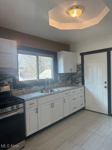 kitchen featuring stainless steel gas stove, white cabinetry, a tray ceiling, and a sink