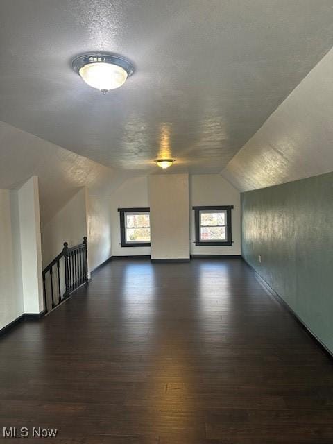 additional living space with dark wood finished floors, lofted ceiling, baseboards, and a textured ceiling