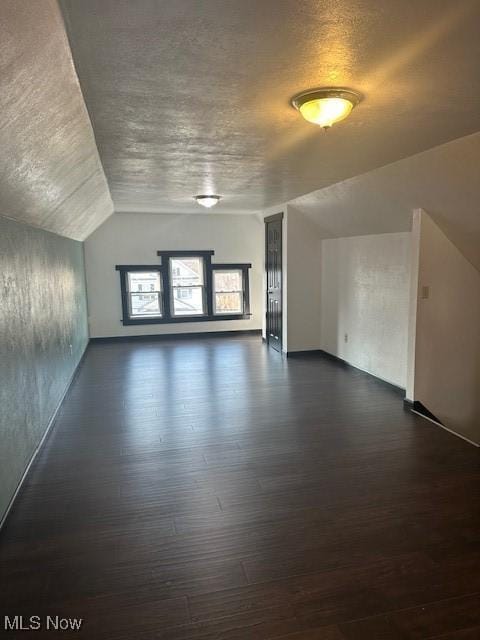 additional living space with dark wood-style flooring, a textured ceiling, and vaulted ceiling