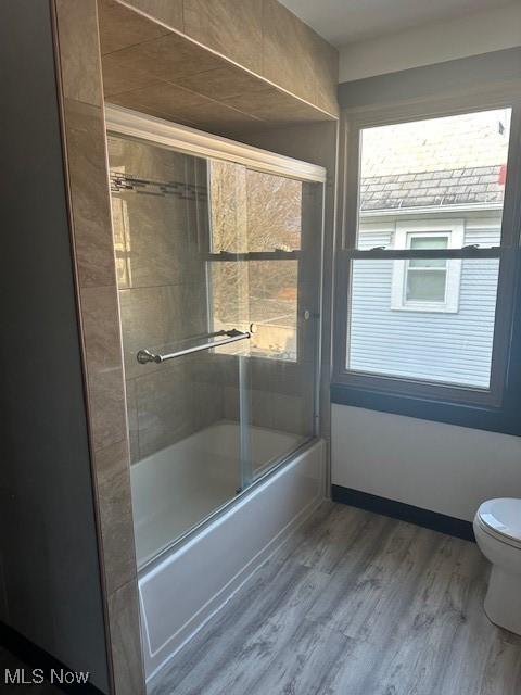 full bathroom featuring toilet, wood finished floors, baseboards, and enclosed tub / shower combo