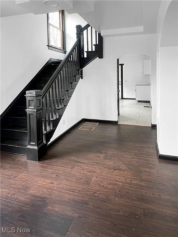 stairway with arched walkways, wood finished floors, and baseboards