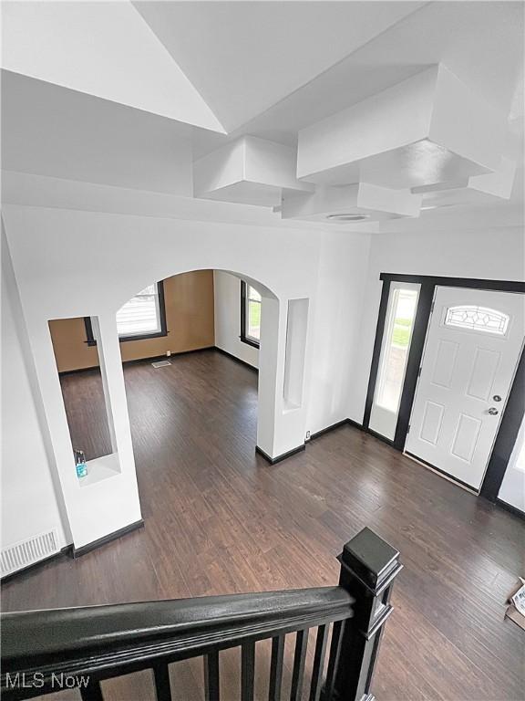 entryway with arched walkways, a wealth of natural light, and dark wood-style floors