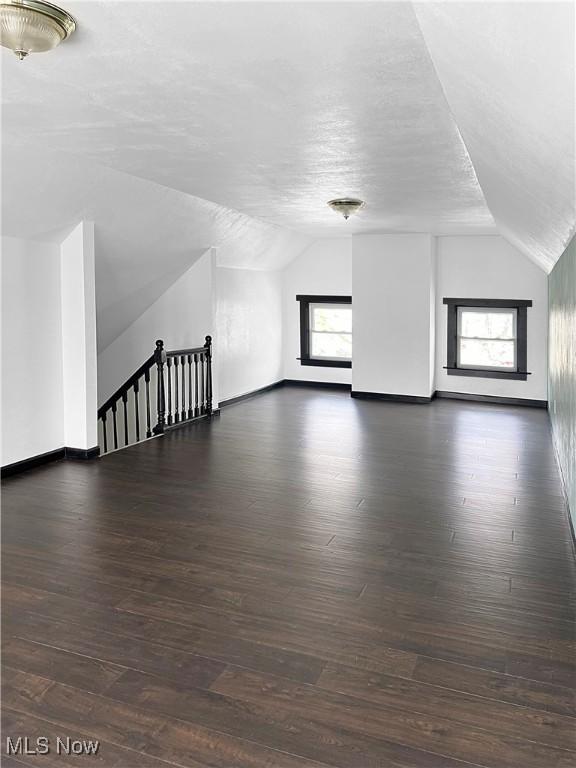 bonus room featuring lofted ceiling, baseboards, dark wood-style floors, and a textured ceiling