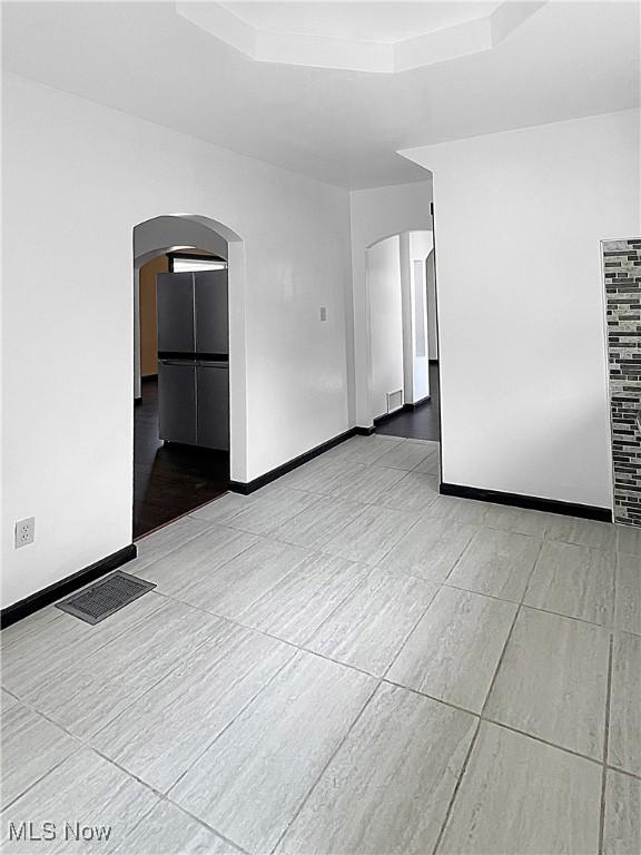 spare room featuring arched walkways, visible vents, and a tray ceiling