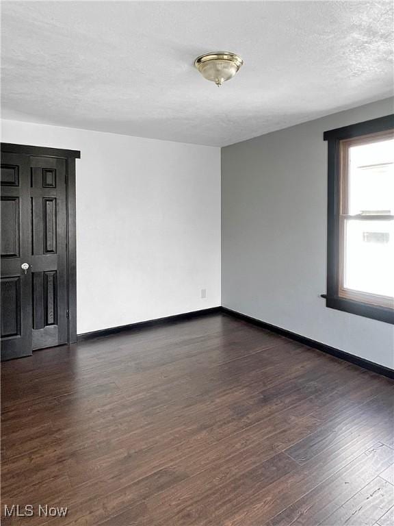 spare room with baseboards, a textured ceiling, and dark wood-style floors