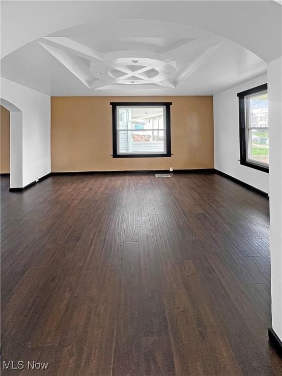 empty room featuring dark wood finished floors, coffered ceiling, and a healthy amount of sunlight