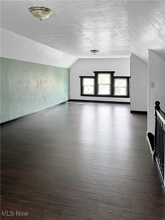 bonus room with lofted ceiling, dark wood-style flooring, a textured ceiling, and baseboards