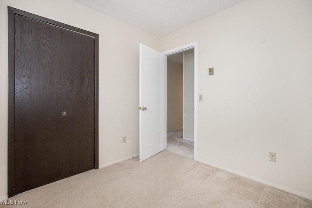 unfurnished bedroom featuring light colored carpet, a closet, and baseboards