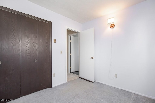 unfurnished bedroom featuring a closet, light colored carpet, and baseboards